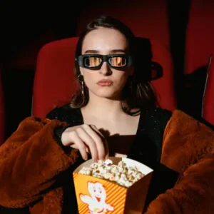 Woman enjoying popcorn in 3D movie theater, wearing 3D glasses.